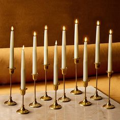 seven candles are lined up in a row on a marble table with a gold cloth behind them