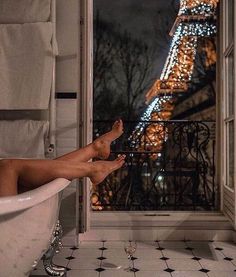 a woman is sitting in a bathtub with the eiffel tower behind her