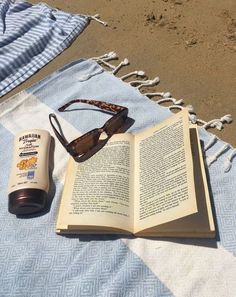 an open book and sunglasses on a beach towel next to a bottle of sunscreen