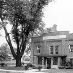 black and white photograph of an old brick building with trees on the side walk in front of it