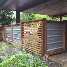 a wooden fence with metal slats on the sides and flowers growing in the foreground