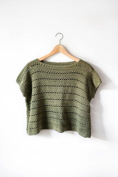 a green knitted top hanging on a white wall with a wooden hanger in front of it