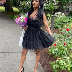 a woman in a short black dress holding flowers