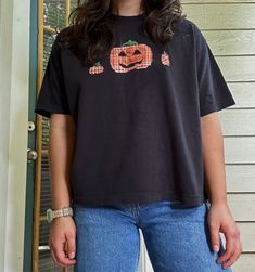 a woman standing in front of a door wearing a black shirt with pumpkins on it