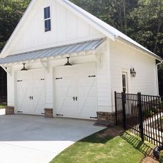 a white garage with two doors and a black gate in front of the garage is surrounded by trees