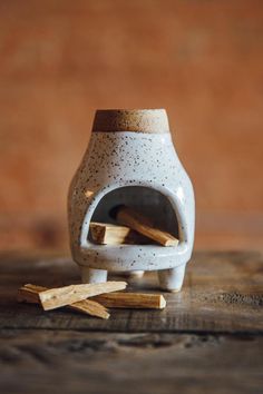 a small white vase with sticks sticking out of it on a wooden table next to some wood