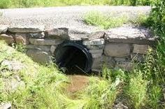 there is a tunnel in the ground with water coming out of it and grass growing around