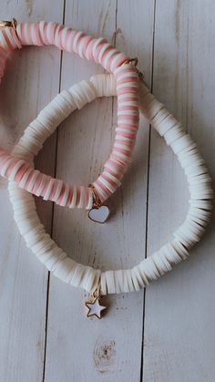 two white and pink bracelets on top of a wooden table next to each other