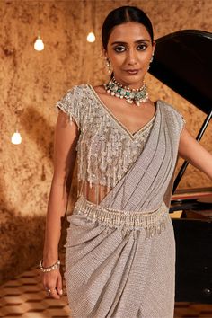 Indulge in glamour with this silver drape sari in lycra, adorned with intricate embroidery. The half-on-side tassels add a playful touch to the ensemble. The outfit is both padded and secured with a hook-eye closure, ensuring a comfortable fit. Complete the look with the embellished belt, adding a chic and stylish accent to this stunning outfit. Party Wear Draped Sharara With Cutdana, Party Sharara With Cutdana And Draped Design, Festive Draped Choli For Eid, Festive Draped Glamorous Blouse Piece, Festive Glamorous Draped Blouse Piece, Festive Draped Sets For Festivals, Festive Draped Sharara With Mirror Work, Diwali Mirror Work Pre-draped Saree, Diwali Silver Pre-draped Saree With Mirror Work