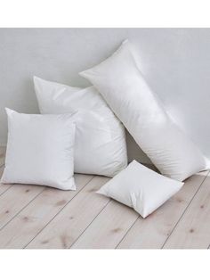 four white pillows sitting on top of a wooden floor next to a lamp and vase