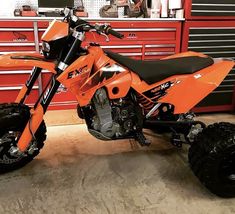 an orange dirt bike parked in front of a red toolbox with tools on it