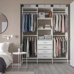 a white closet with drawers and clothes hanging on the wall, next to a bed