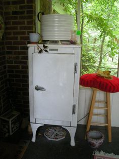 an old white refrigerator sitting in front of a window next to a potty chair