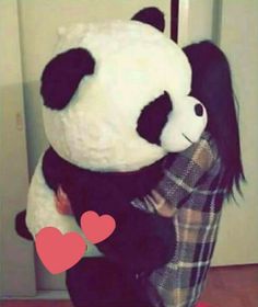 a person hugging a giant panda bear with a heart on it's chest in front of a refrigerator