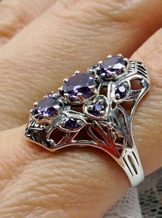 Art Deco 1930s Amethyst 9-Gem Ring9Gem Ring Design#D69 Give your wardrobe the stylish edge it needs with the Amethyst 9-Gem Ring. This stunning vintage Art Deco ring is crafted from sterling silver, making it just as timeless as its design. The piece is set with three captivating center 6mm round cut Purple/Amethyst CZ gemstones and six more 2mm gemstones that adorn the sides of the setting. A unique filigree silver band completes this work of art to perfections - an impressive reminder of the g Purple Anniversary Rings With Intricate Design, Vintage Amethyst Crystal Ring With Gemstone Detail, Vintage Amethyst Crystal Ring With Gemstone, Vintage Amethyst Ring With Accent Stones For Anniversary, Vintage Purple Sapphire Gemstone Ring, Art Deco Purple Amethyst Ring For Anniversary, Vintage Purple Amethyst Ring For Anniversary, Purple Amethyst Art Deco Ring For Anniversary, Vintage Amethyst Ring With Accent Stones