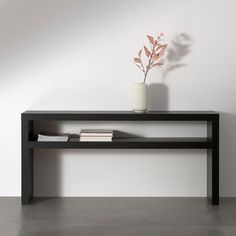 a vase with a plant on top of it next to a black shelf that holds books