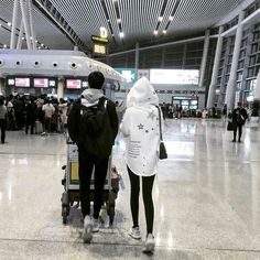 two people are walking through an airport with luggage on their backs and one person is pushing a stroller