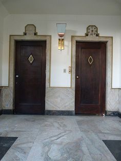 two brown doors in a room with black and white floor tiles on the walls, and an ornate light fixture above them