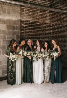 a group of women standing next to each other in front of a brick wall holding bouquets