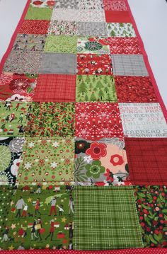 a quilted table runner made with red and green fabric, featuring christmas themed designs