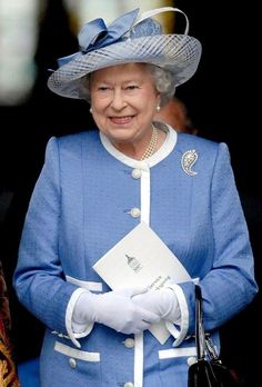 the queen of england is wearing a blue suit and hat with white gloves on it