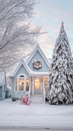 a small blue house with a wreath on the front door and trees covered in snow