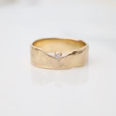 a gold ring with a diamond in the center on a white surface, ready to be worn