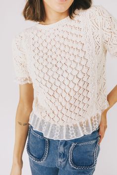 a woman wearing jeans and a crochet top with her hands on her hips