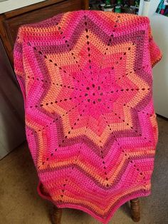 a pink crocheted blanket sitting on top of a wooden chair