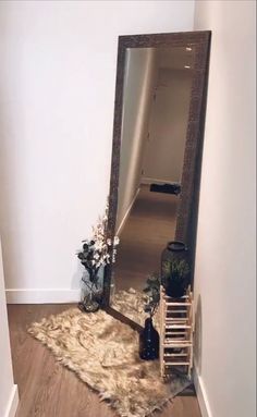 a large mirror sitting on top of a wooden floor next to a vase with flowers