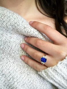 a woman's hand with a blue ring on her finger and a white sweater