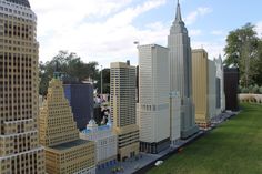 a model of a city with tall buildings and people walking on the grass in front of it