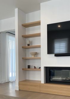 a television mounted on the wall above a fireplace in a room with white walls and wooden shelves