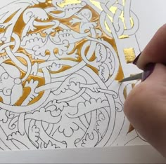 a person is drawing on paper with gold foil