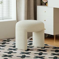 a white stool sitting on top of a rug in front of a dresser and window