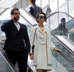 a man and woman walking down an escalator talking on their cell phones while holding hands