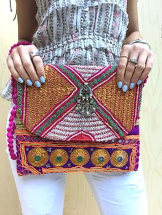 Our new bold embellished clutches come in new statement square shape and are beautiful handmade by local artisans of the Banjara tribe in India. Embellished with bold metallic thread these bags are a stunning accessory to any outfit. All bags are hand-crafted using patchworks of vintage Banjara embroidery and embellishments. According to some authorities, the Banjara lineage goes back some 2000 years. Wear as an over-sized clutch or on your shoulder with the light-weight cotton pompom chain.  Be Artisan Multicolor Rectangular Clutch, Bohemian Clutch With Handwork, Bohemian Clutch Shoulder Bag For Festivals, Bohemian Rectangular Clutch For Festival, Bohemian Embroidered Clutch For Festive Occasions, Bohemian Embroidered Rectangular Clutch, Bohemian Multicolor Rectangular Clutch, Handmade Multicolor Rectangular Clutch, Handmade Bohemian Clutch For Festive Occasions