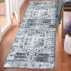 a blue and white rug on the floor next to a vase with purple flowers in it