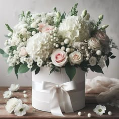 a bouquet of white and pink flowers in a round box with ribbon on the table