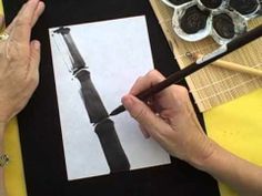 a woman is drawing an image on a piece of paper with a brush and watercolor pencil