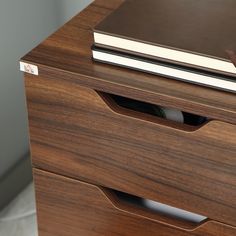 a close up of a wooden drawer with a book on the top and a pen in it