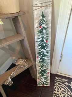 a christmas tree painted on a wooden board next to a step ladder and potted plant