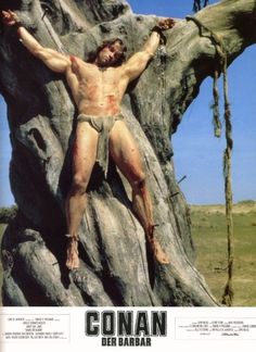 a man with no shirt on standing in front of a tree trunk wearing a cross