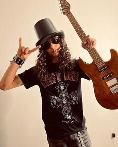 a man with long hair wearing a black hat and holding two guitars in his hands