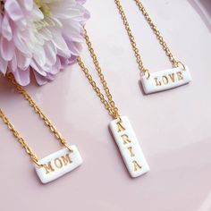 three necklaces with the words mom and love written on them, sitting next to a flower