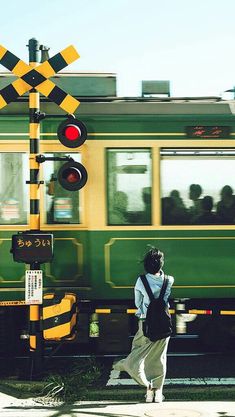 a woman walking down the street in front of a green and yellow train passing by