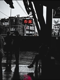 two people sitting on a bench in the rain under a street sign that reads 555