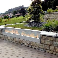 a fire pit sitting on top of a wooden deck next to a lush green hillside