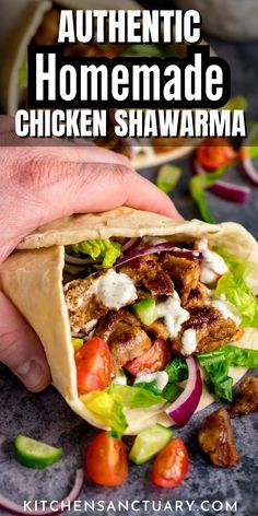 a hand holding a chicken shawarma with lettuce and tomatoes on the side