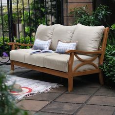 a wooden couch sitting on top of a patio next to a lush green plant filled garden